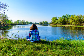 Obraz premium Lonely young woman sitting on a bank of the river