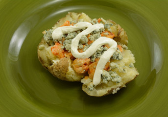 Single serving of stuffed baked potato with hot spicy chicken, blue cheese and sour cream on green plate