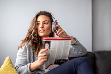 Woman with headphones listening music with headphonese over her head and read magazine on room