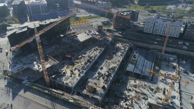 Aerial Top Down Drone Footage of an Industrial Construction Yard in the Process of Building Houses. In the Background with Modern City on a Bright Sunny Day.