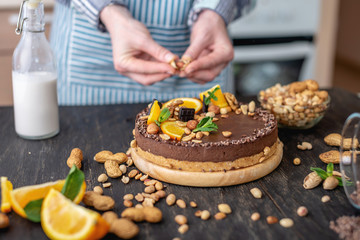 Confectioner decorates chocolate cake with orange and mint leaves with nuts. Concept healthy raw desserts for vegan food