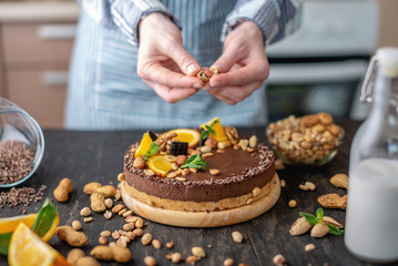 Obraz na płótnie Canvas Confectioner decorates chocolate cake with orange and mint leaves with nuts. Concept healthy raw desserts for vegan food