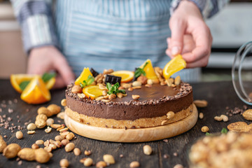 Confectioner decorates chocolate cake with orange and mint leaves with peanuts. Healthy raw desserts for vegan food