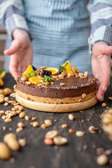 Confectioner decorates chocolate cake with orange and mint leaves with peanuts. Healthy raw desserts for vegan food