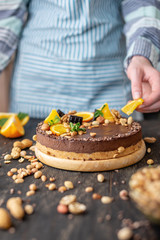 Confectioner decorates chocolate cake with orange and mint leaves with peanuts. Healthy raw desserts for vegan food
