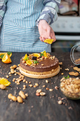 Confectioner decorates chocolate cake with orange and mint leaves with peanuts. Healthy raw desserts for vegan food