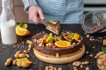 Pastry chef in hand holding a piece of chocolate cake with orange, mint and nuts. Healthy raw desserts for vegan food