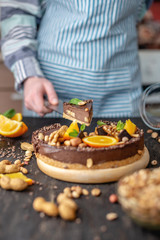 Obraz na płótnie Canvas Pastry chef in hand holding a piece of chocolate cake with orange, mint and nuts. Healthy raw desserts for vegan food