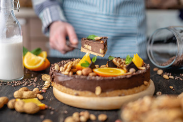Pastry chef in hand holding a piece of chocolate cake with orange, mint and nuts. Healthy raw desserts for vegan food