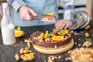 Pastry chef in hand holding a piece of chocolate cake with orange and peanuts. Healthy raw desserts for vegan food