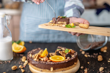 Hand breaks with a fork a piece of chocolate cake with orange and nuts. Concept healthy raw desserts for vegan food