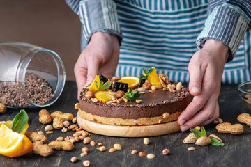 Hands decorated with chocolate cake orange and mint leaves with peanuts and nuts. Healthy raw desserts for vegan food