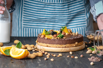 Confectioner decorates chocolate cake with orange and mint leaves with nuts. Healthy raw desserts for vegan food
