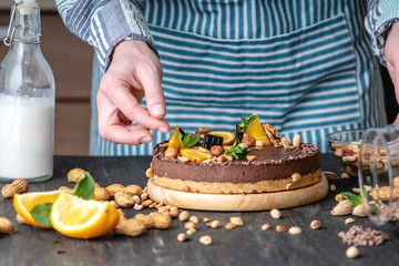 Confectioner decorates chocolate cake with orange and mint leaves with nuts. Healthy raw desserts for vegan food