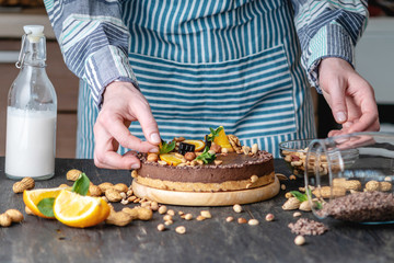 Confectioner decorates chocolate cake with orange and mint leaves with nuts. Healthy raw desserts for vegan food