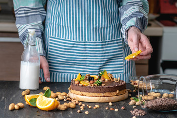 Confectioner decorates chocolate cake with orange and mint leaves with nuts. Healthy raw desserts for vegan food