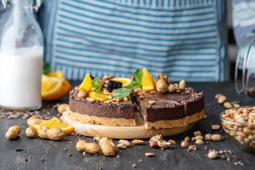 Confectioner decorates chocolate cake with orange and mint leaves with nuts. Concept healthy raw desserts for vegan food