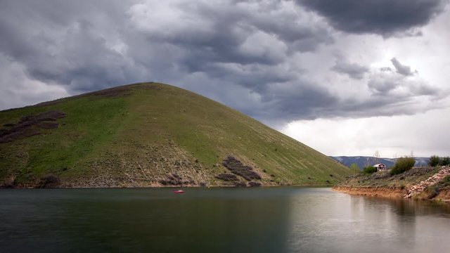 Time lapse of thick dark clouds moving Deer Creek Reservoir  past grassy green hill in Utah.