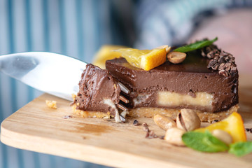 Hand breaks with a fork a piece of chocolate cake with orange, mint leaves and nuts. Healthy raw desserts for vegan food