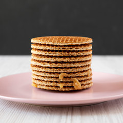 Stack of homemade Dutch stroopwafels with honey-caramel filling on a pink plate, side view. Close-up.