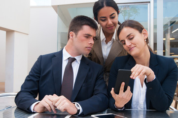 Smiling business woman showing smartphone screen to colleagues. Business man and women reading news, standing and sitting at cafe table. Business news concept. Front view.