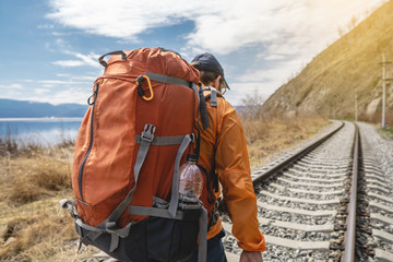 Tourist Hiking with an orange backpack is on the old railway at the foot of the mountain. Travel to...