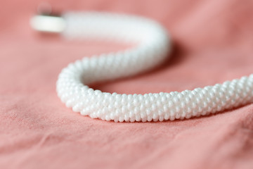 White beaded necklace on a textile background coral color close up