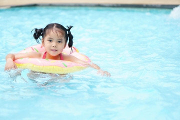 Fototapeta na wymiar Asian child cute or kid girl swimming wear life ring because can not swim and smile with happy fun on swimming pool or water park for fresh relax with exercise at summer holiday travel in hotel resort