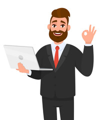 Happy bearded business man holding/showing a latest new laptop and gesturing/making okay or OK sign with hand fingers while winking eye. Modern technology, digital device/gadget concept in cartoon.