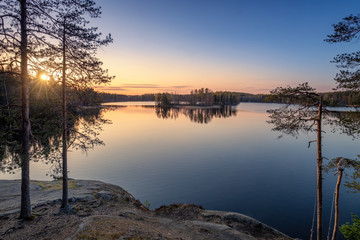 Obraz na płótnie Canvas Scenic landscape with sunset, peaceful lake and tree roots at calm spring evening in Finland