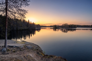 Fototapeta premium Scenic landscape with sunset, peaceful lake and tree roots at calm spring evening in Finland