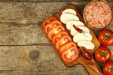 Fresh Mozzarella cheese and tomatoes onkitchen cutting board. Healthy diet food. Chili peppers with cheese.