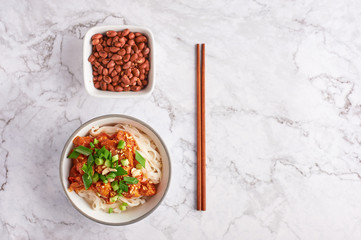shan noodles with peanuts and chopsticks at white marble tabletop. burmese cuisine traditional dish. myanmar food. rice noodles with pork in tomatoes. copy space. top view