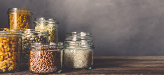 Various raw cereals, grains, beans and pasta for cooking healthy food in glass jars on a wooden...