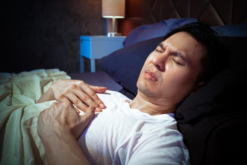 asian man has a heart attack symptoms while sleeping on bed at night