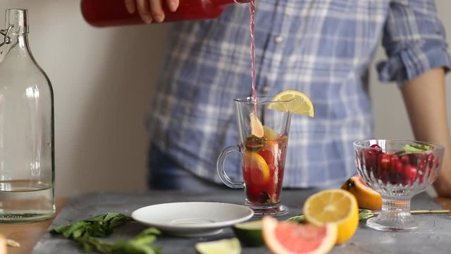 Woman preparing a delicious summer red strawberry cocktail on the table in the kitchen with cranberries and grapefruit, closeup. Summer, refreshing drinks