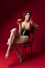Medieval redhead young woman as a duchess in black corset and night clothes sitting on a chair on...