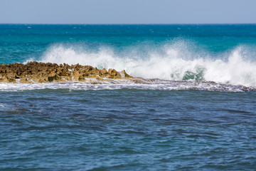 Onde spumeggianti che si infrangono sulla costa rocciosa e il mare blu