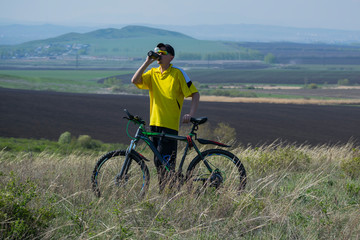 Obraz premium A man on a bicycle stopped on a hill and drinks water.
