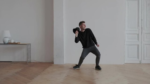 Young guy have fun at home. He dancing on the white wall background. He is flexi and playful. Man drops his hat in expressive dance. Modern choreographer rehearsing his authors dance indoor.