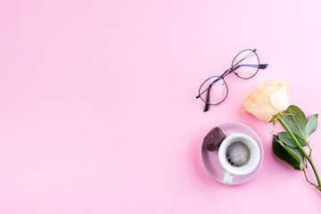 Fresh cup of coffee, glasses and a beige fragrant roses on a pastel pink background, flat lay