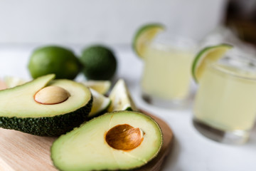 Fresh avocado, lime, drink and nacho chips lying on marble background. Recipe for Cinco de Mayo party