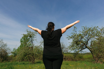 Fototapeta na wymiar Body positive, freedom, high self esteem, confidence, happiness, obesity. Overweight woman rising hands towards the sky contemplating outdoors.