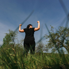 Fototapeta na wymiar Body positive, freedom, high self esteem, confidence, happiness, obesity. Overweight woman rising hands towards the sky contemplating outdoors.