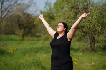 Body positive, freedom, high self esteem, confidence, happiness, obesity. Overweight woman rising hands towards the sky contemplating outdoors.