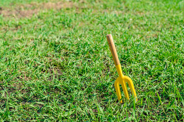 Small garden tool on grass background. Little yellow fork.