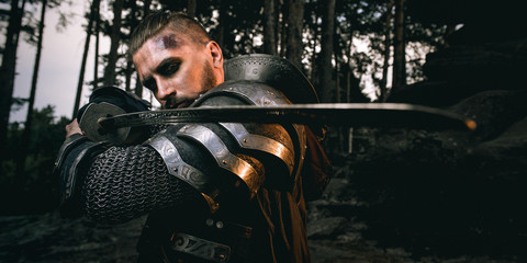 Fototapeta na wymiar mystery scarface knight in armor with sword and crossbow in the forest