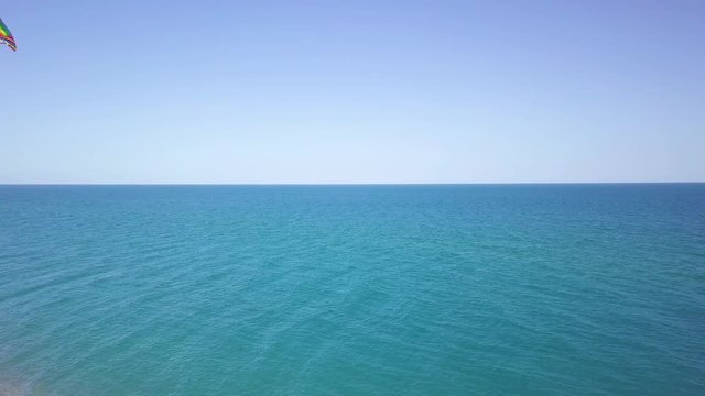 Aquilone colorato che vola in spiaggia con sfondo del mare blu.