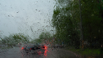 Blurred road through the windshield of a car in the rain. Drops of shower on the glass. Driving in bad weather