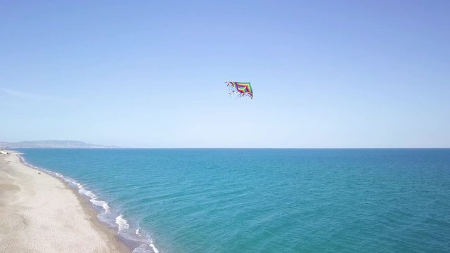 Aquilone colorato che vola in spiaggia con sfondo del mare blu.